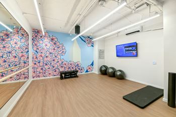 A yoga studio with a wooden floor and a wall with a screen and exercise balls